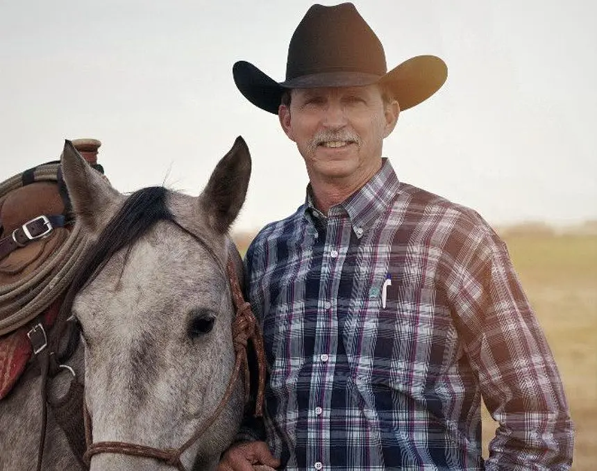 A man in plaid shirt and cowboy hat standing next to horse.